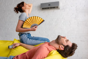 lying man with closed eyes and woman with hand fan suffering from heat at home
